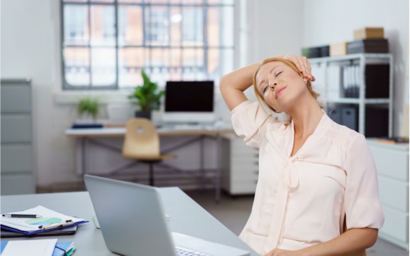 žena precvičujúca si krčnú chrbticu sediac v práci za počítačom